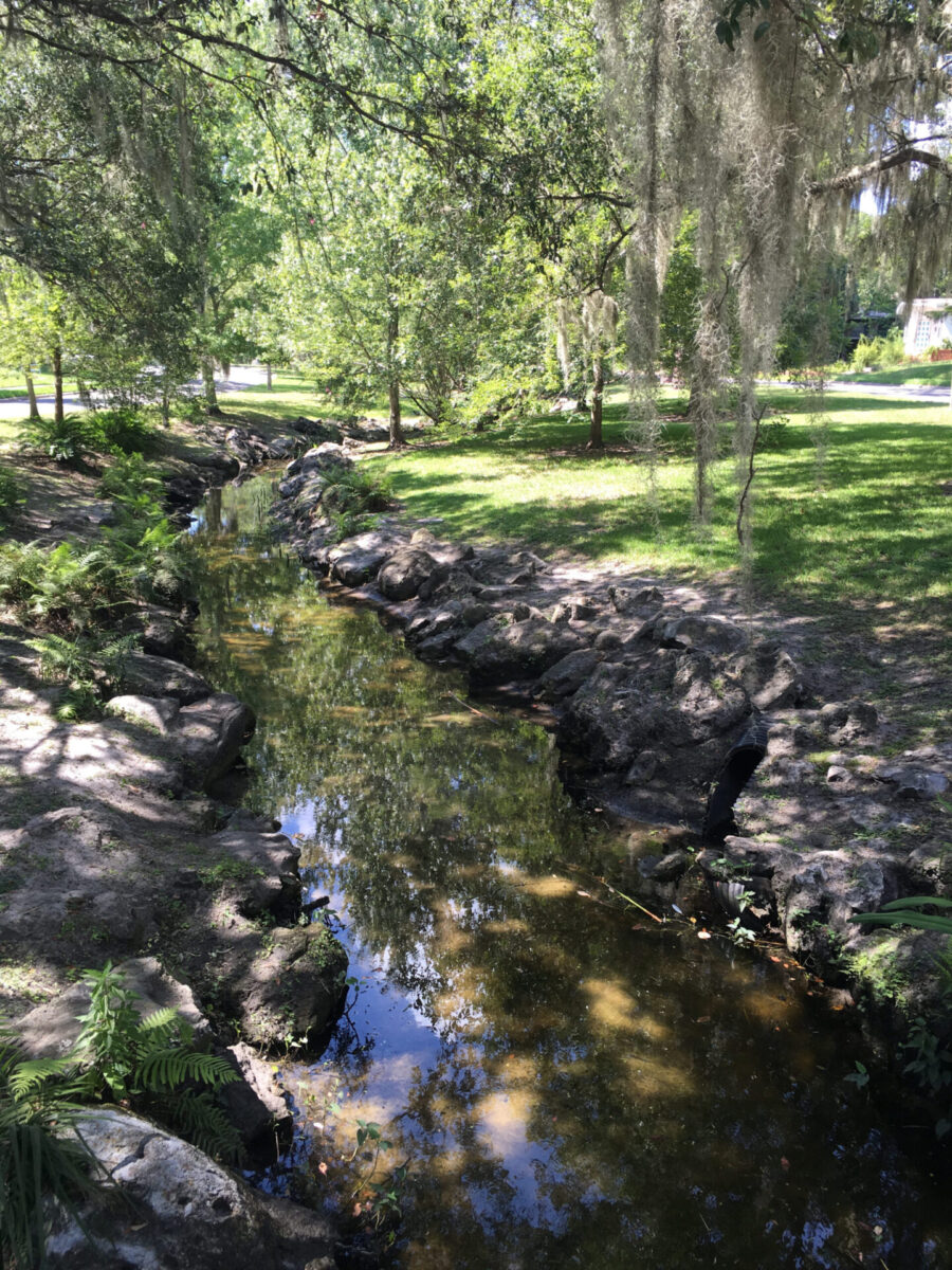 The Sweetwater waterway passes through tree-shaded grassy banks in a neighborhood.